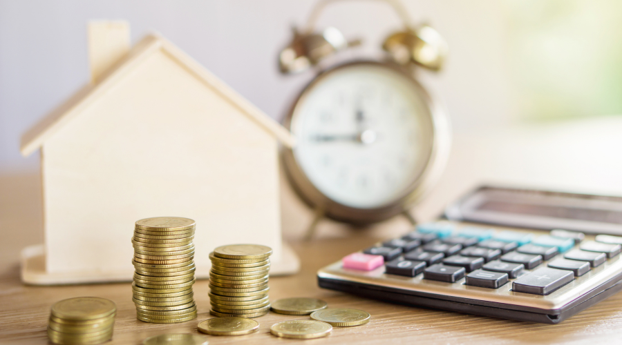 House model, coins, calculator, and clock on table.